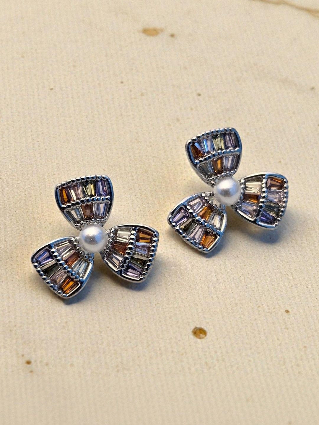 Close-up of silver rhodium-tone flower stud earrings showing amber, lilac and smoky CZ stones on cream fabric