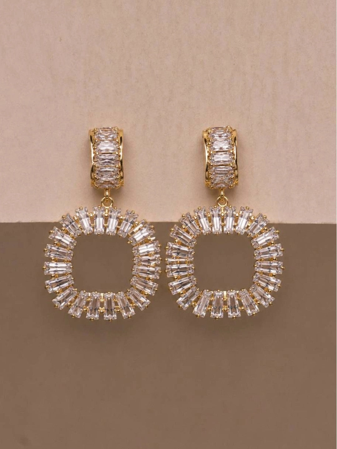 Pair of gold-plated circular drop earrings with baguette CZ stones on beige background