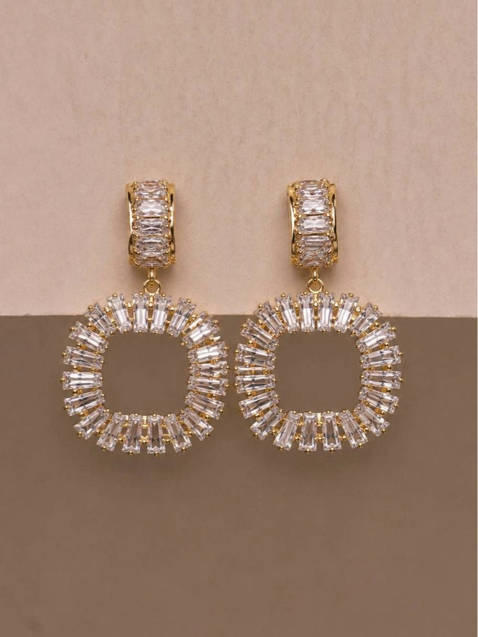 Gold-plated baguette CZ earrings showing circular and square pendant styles on pink surface