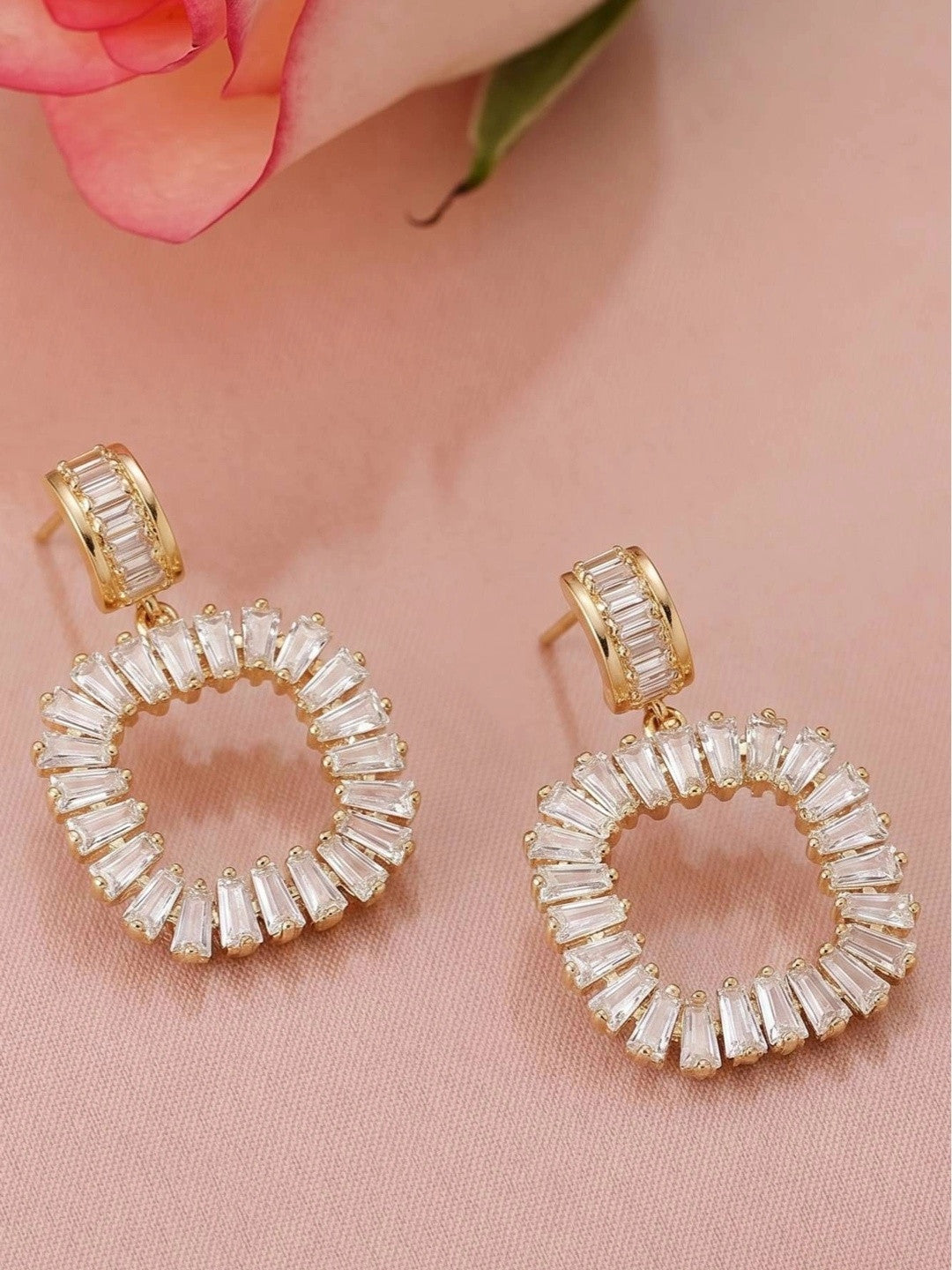 Close-up pair of gold-plated circular baguette CZ drop earrings on pink fabric