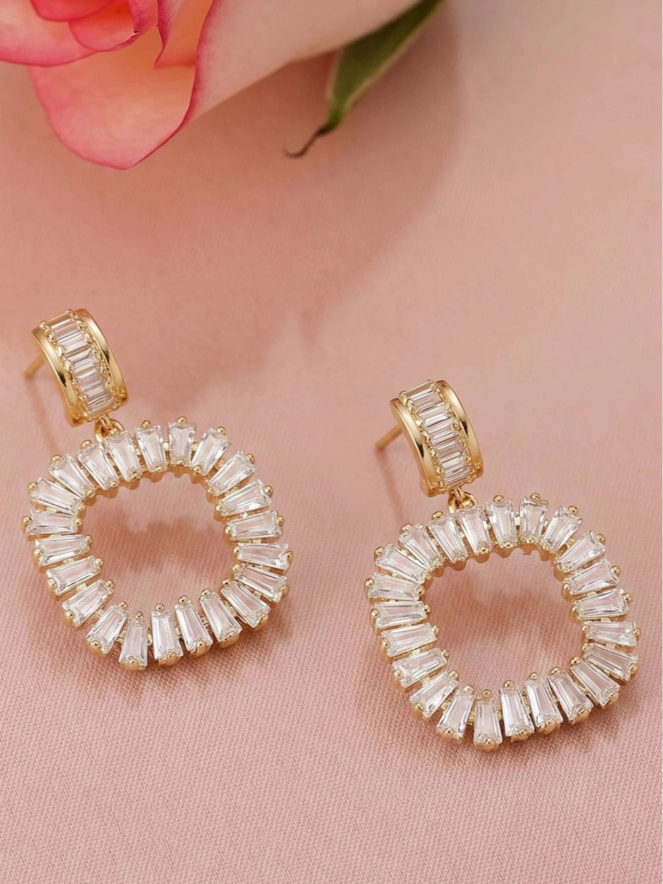 Close-up pair of gold-plated circular baguette CZ drop earrings on pink fabric