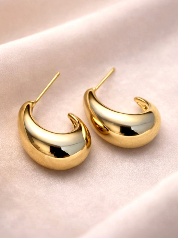 Pair of gold-plated chunky crescent hoop earrings with post backs on blush satin fabric