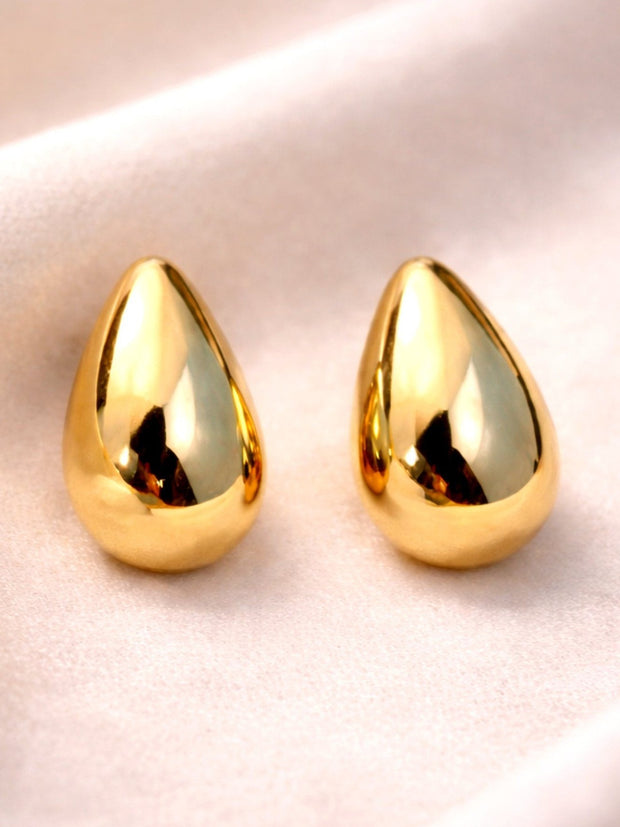 Two gold-plated puffy teardrop stud earrings with mirror finish on blush satin background