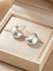 Pair of brushed silver teardrop hoop earrings resting in a cream jewellery box