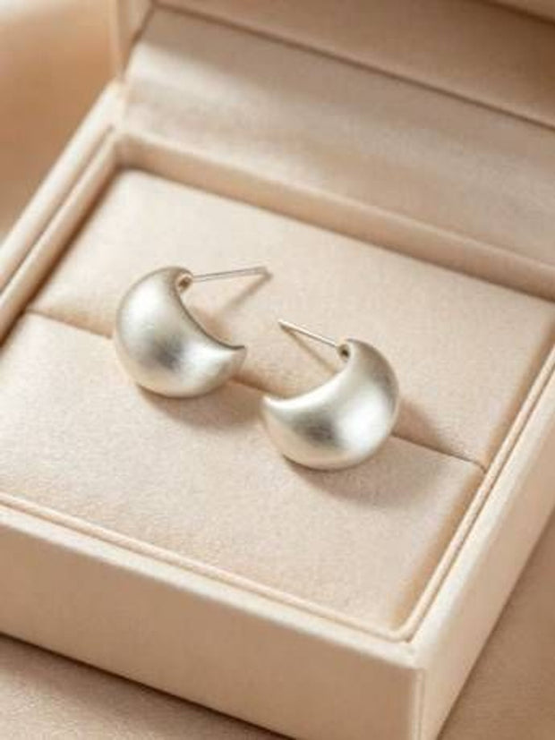 Pair of brushed silver teardrop hoop earrings resting in a cream jewellery box