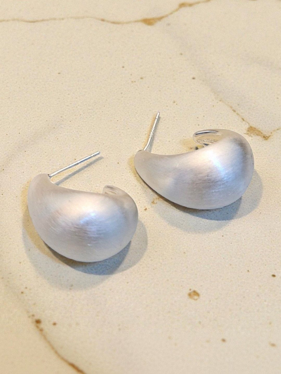 Two brushed silver dome teardrop earrings with stud posts on a marble surface