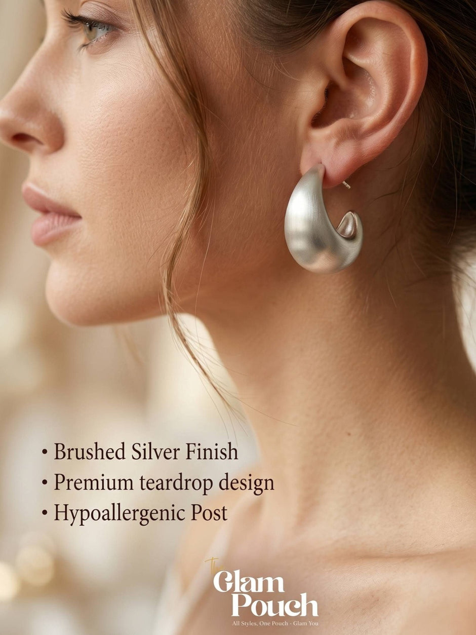 Woman wearing a large brushed silver teardrop hoop earring shown in profile close-up