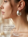 Woman wearing a large brushed silver teardrop hoop earring shown in profile close-up