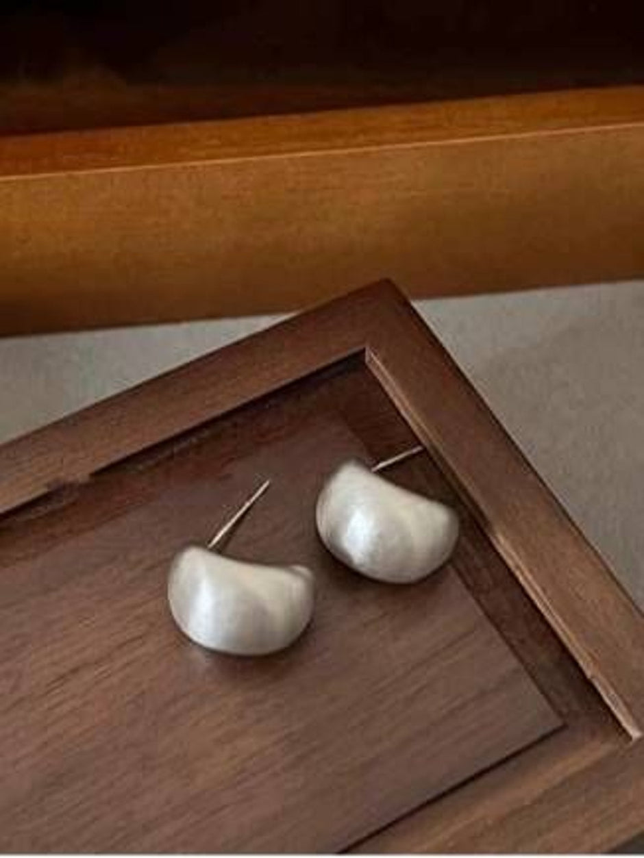 Pair of silver brushed crescent dome earrings placed on a dark wooden tray