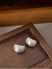 Pair of silver brushed crescent dome earrings placed on a dark wooden tray