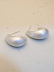 Brushed silver teardrop stud hoops lying flat on a white speckled surface