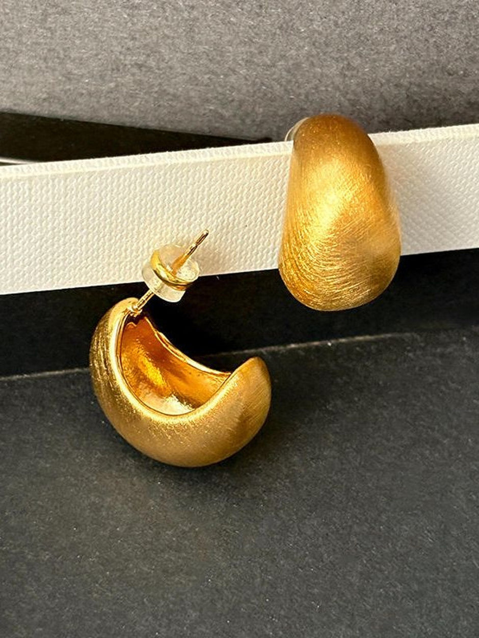 Close-up of one matte gold chunky hoop earring showing brushed texture and push-back post closure on dark grey surface