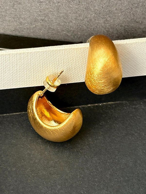 Close-up of one matte gold chunky hoop earring showing brushed texture and push-back post closure on dark grey surface