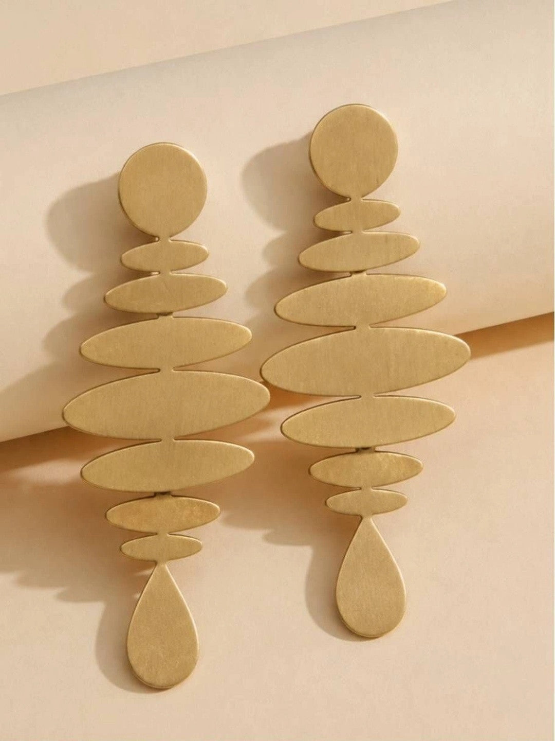 Two matte gold graduated oval disc earrings lying flat on a cream paper background showing full length