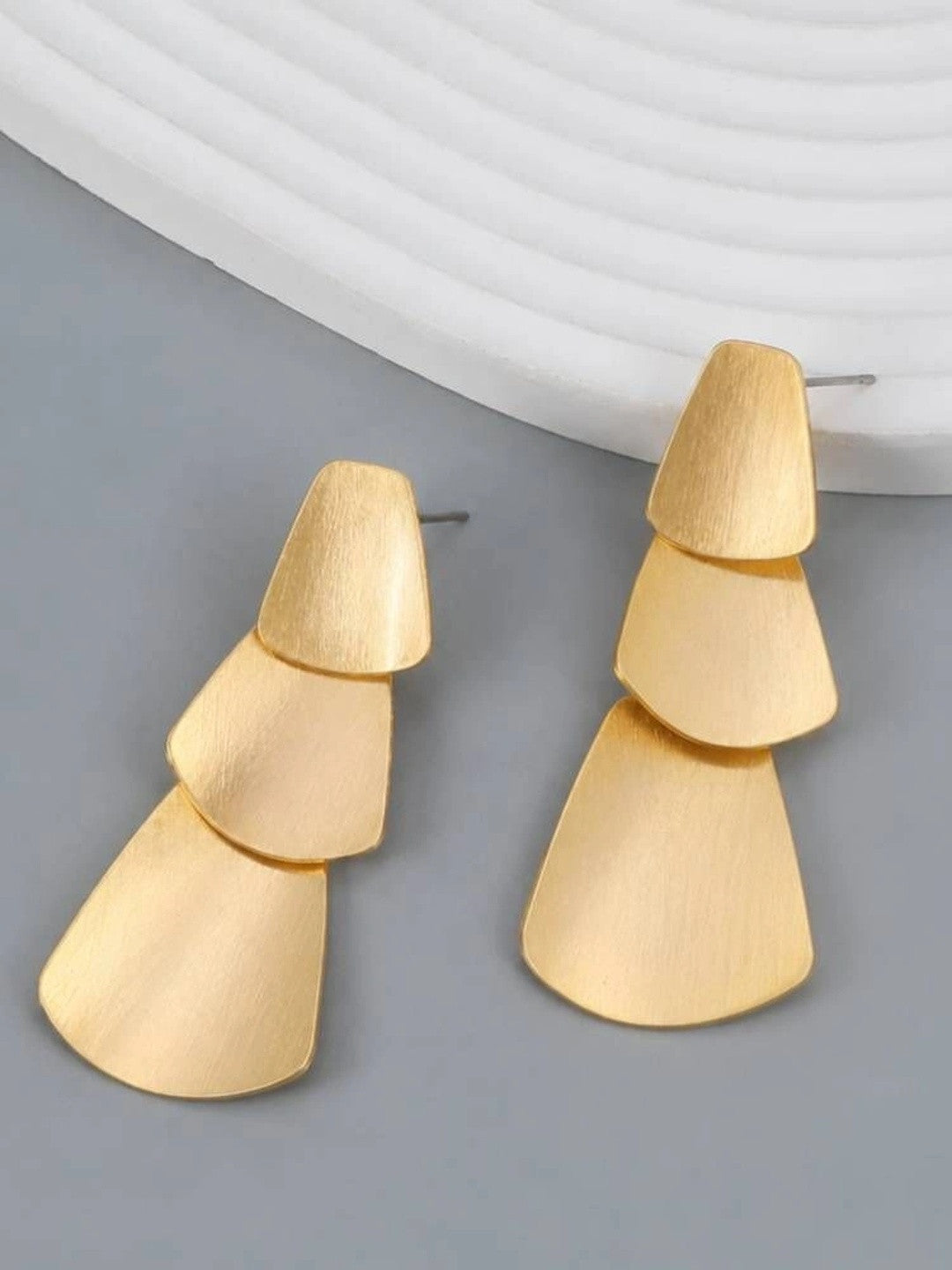 Both matte gold tiered trapezoid drop earrings standing upright side by side on grey background