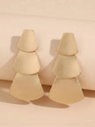 Two brushed gold geometric tiered drop earrings leaning against a beige cylindrical prop
