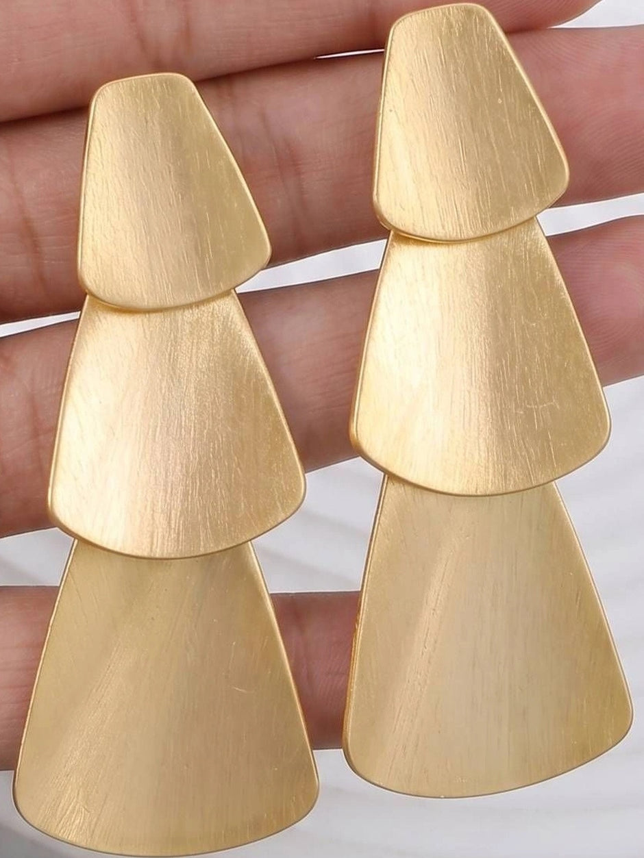 Close-up of gold-toned three-tier geometric drop earrings held in a hand showing brushed matte texture