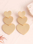Pair of matte gold triple heart drop earrings laid flat on a pink marble surface