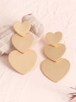 Two matte gold triple heart drop earrings displayed against a white stone and pink background