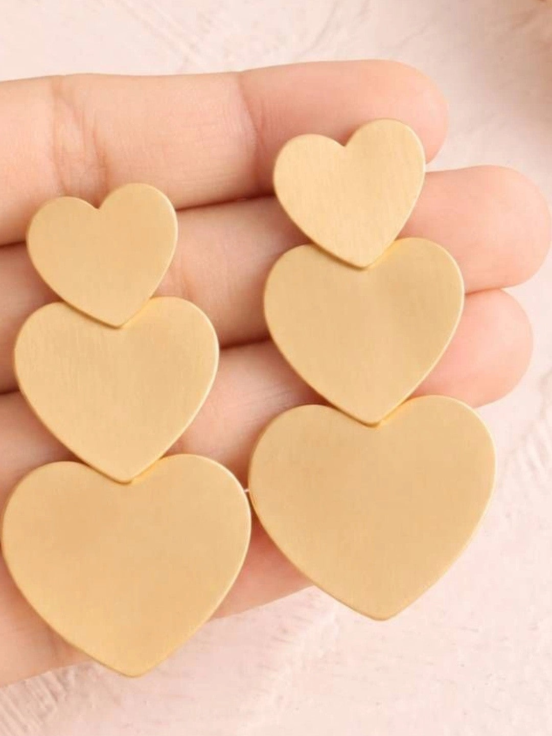 Both matte gold triple heart earrings resting on an open palm showing size and scale