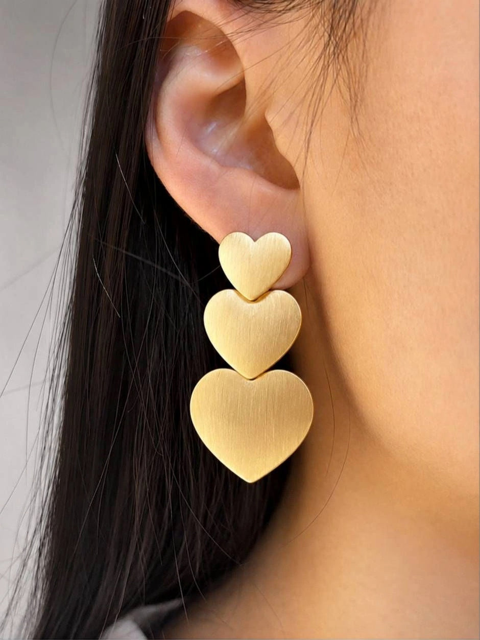Matte gold triple heart drop earring worn on a woman's ear showing full length and drape
