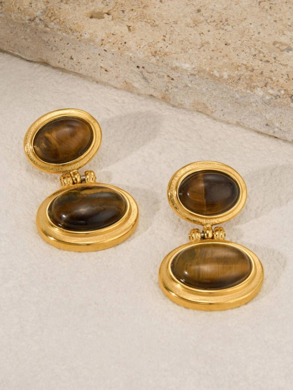 Front view of both gold-plated tiger eye oval drop earrings laid flat on a beige surface