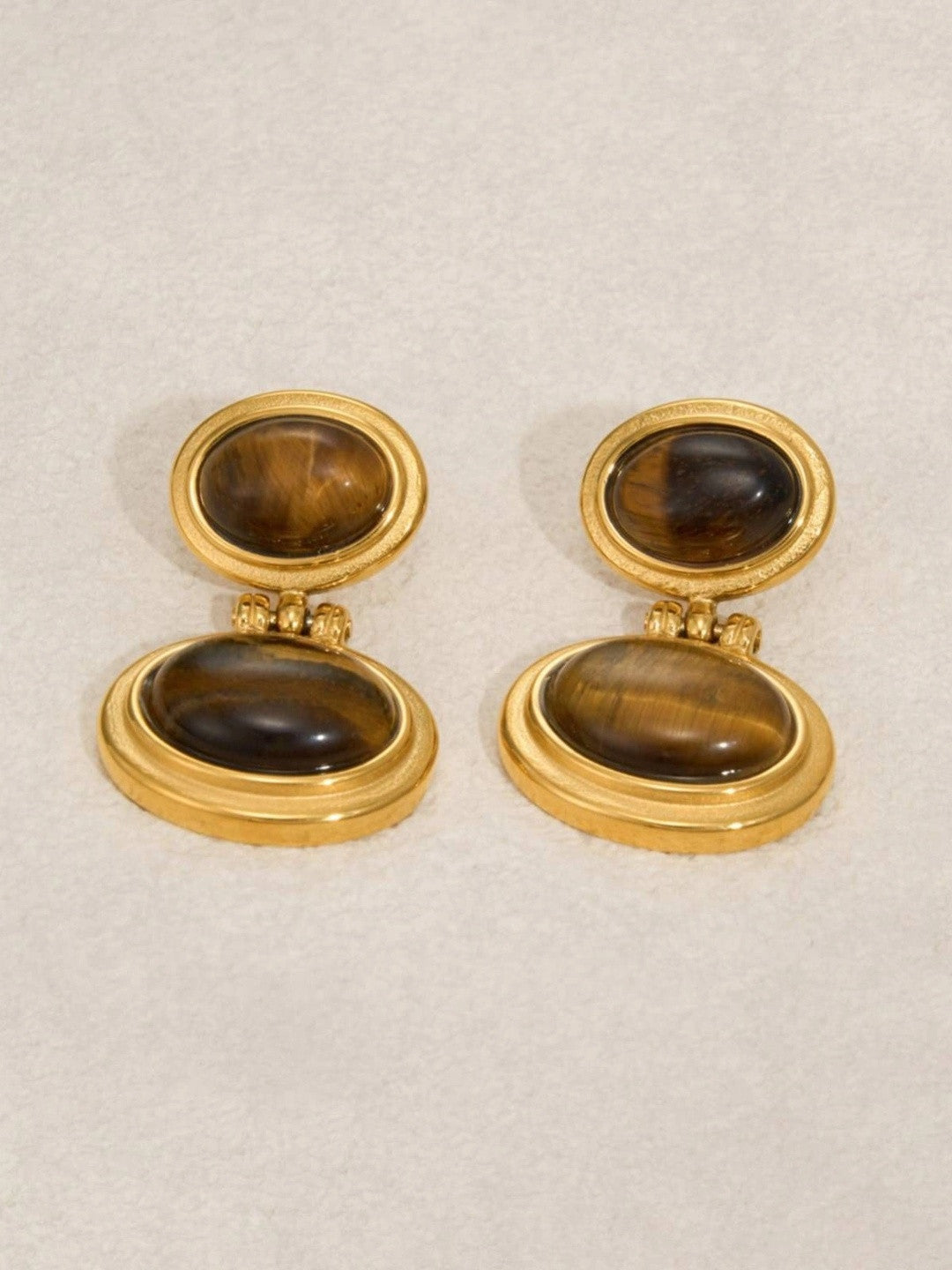 Straight-on flat lay of both gold-plated tiger eye oval drop earrings on a neutral background