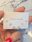 Hand holding a white jewellery card displaying three pairs of silver CZ earrings against a marble background