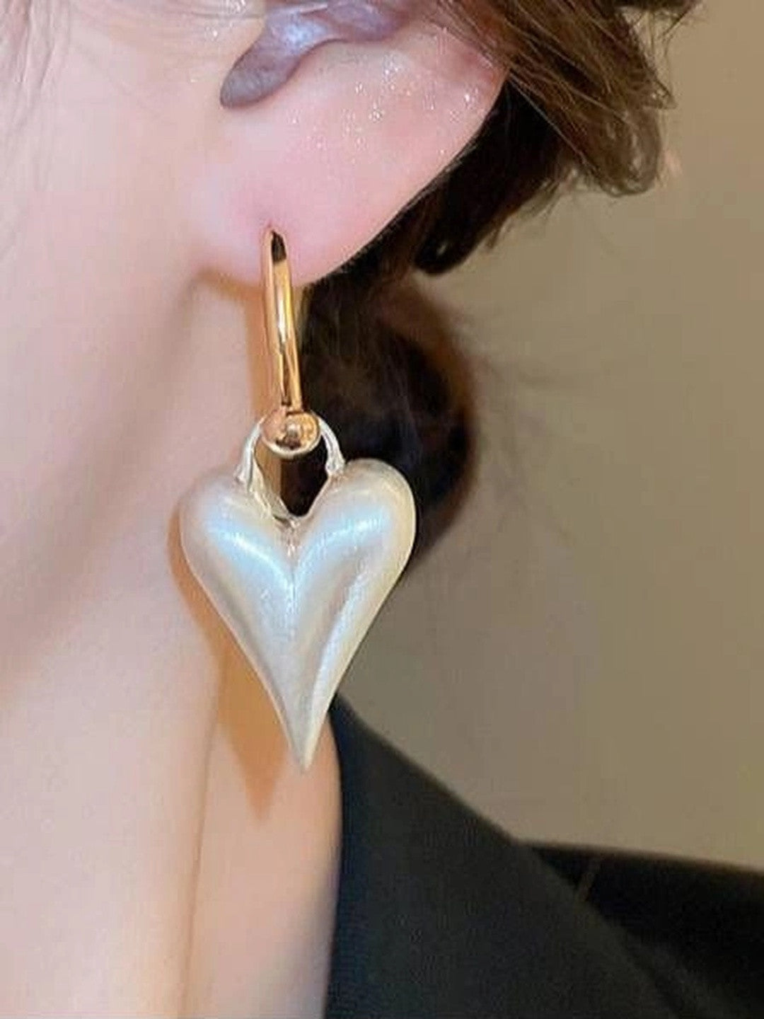 Close-up of a pearl-finish heart drop earring worn on a model's ear with brown hair