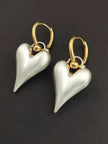 Two pearl-white puffy heart drop earrings with gold ball detail on a dark grey background