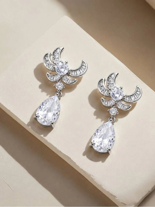 Both CZ crescent-wing drop earrings laid flat on a cream stone surface showing top and pendant