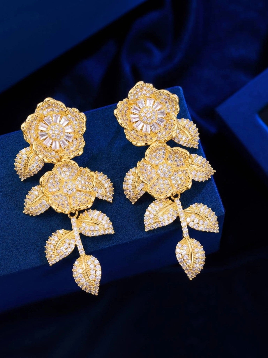 Pair of gold-plated floral CZ drop earrings displayed front-side-up on a blue velvet box