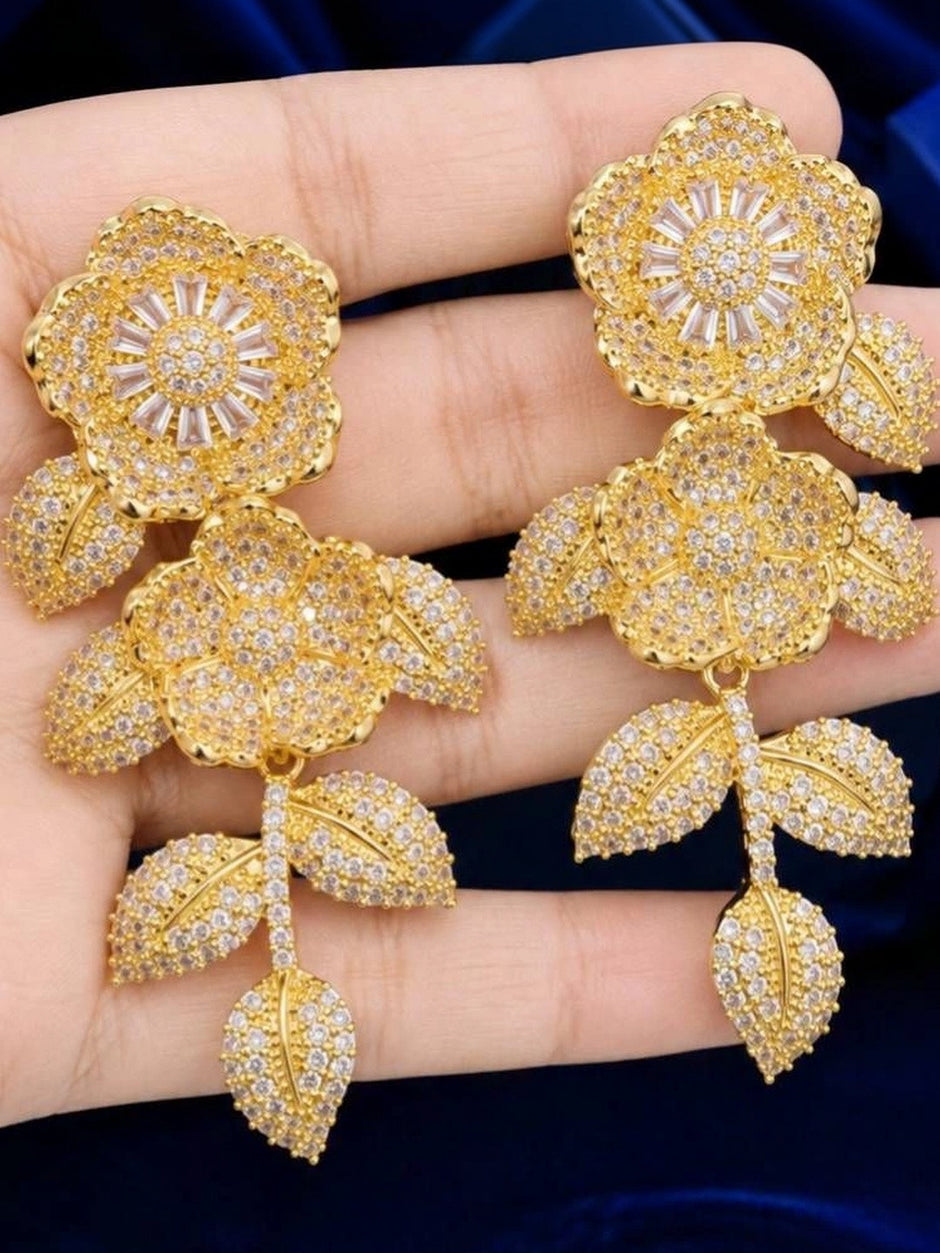 Pair of gold-plated floral CZ drop earrings held flat on an open palm showing size and detail