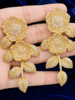 Pair of gold-plated floral CZ drop earrings held flat on an open palm showing size and detail