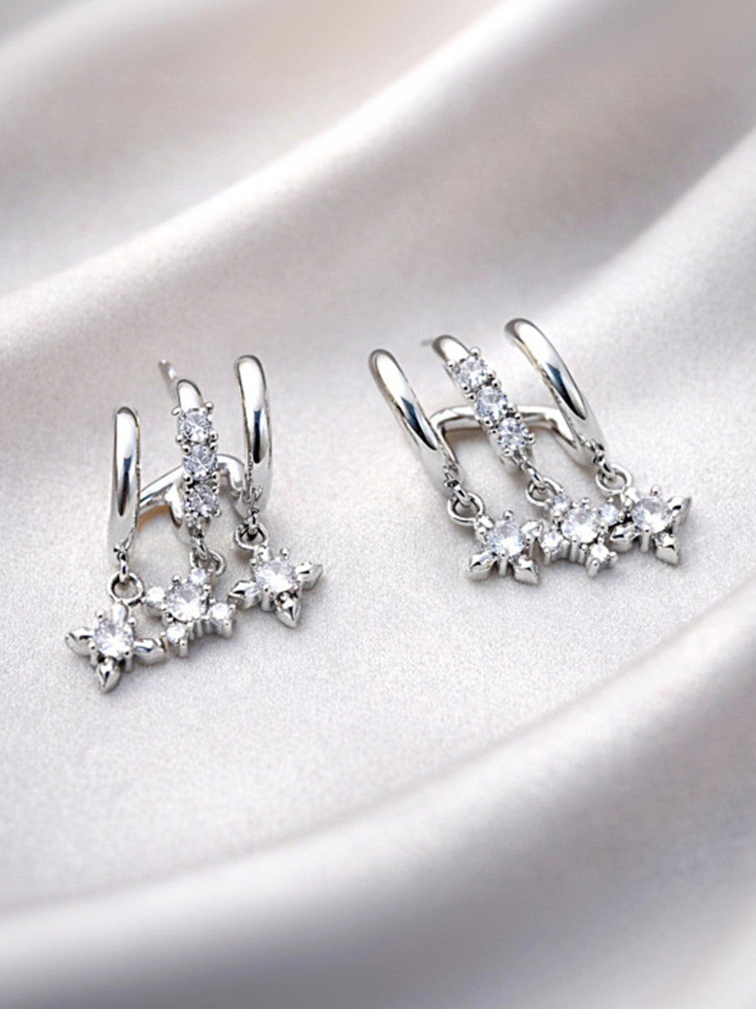 Pair of silver double hoop earrings with three CZ star charms laid on white satin fabric