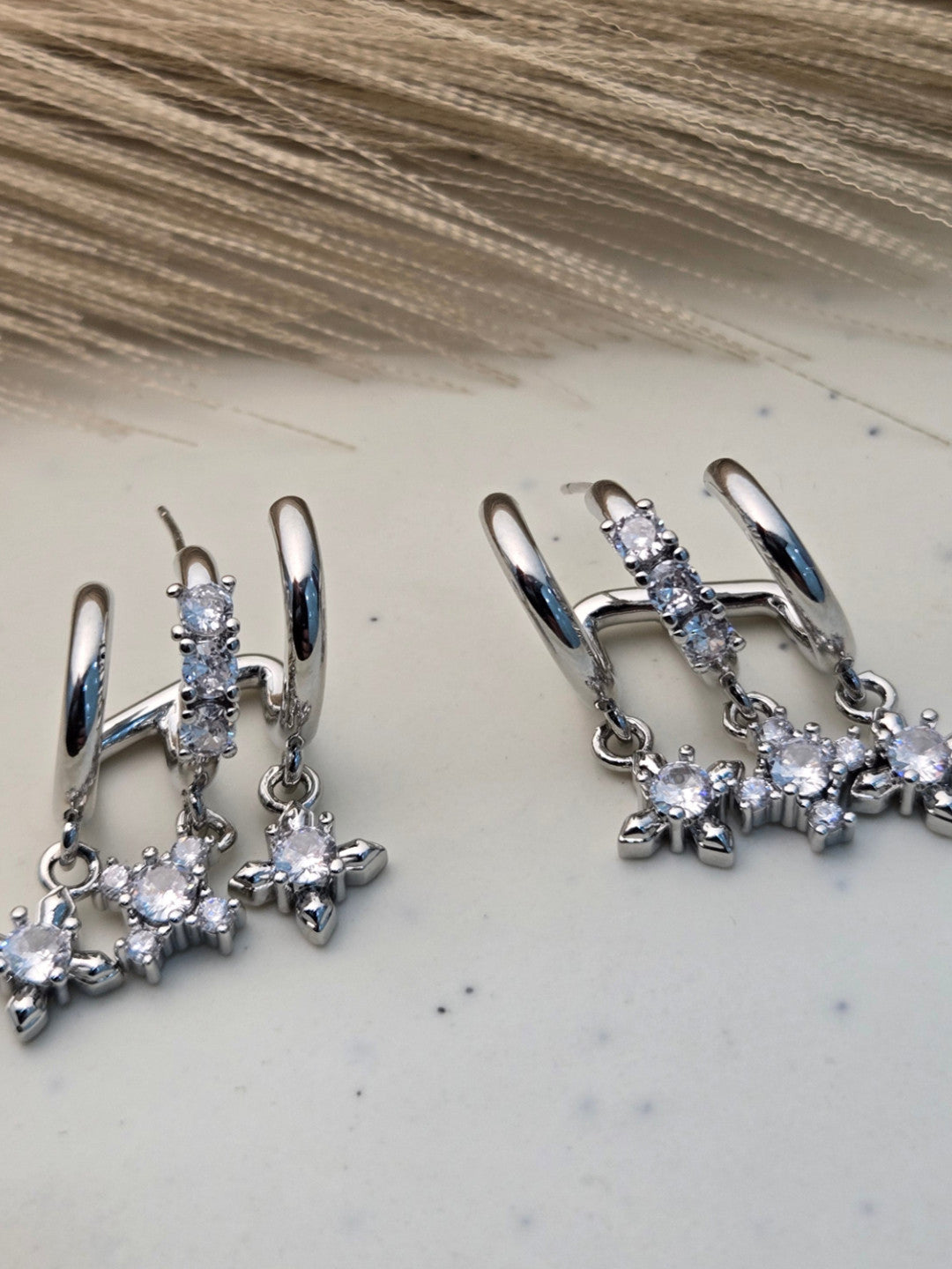 Close-up of both silver CZ star charm double hoop earrings placed on a marble surface