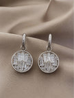 Pair of silver circular drop earrings with baguette crystal clusters on a beige fabric background
