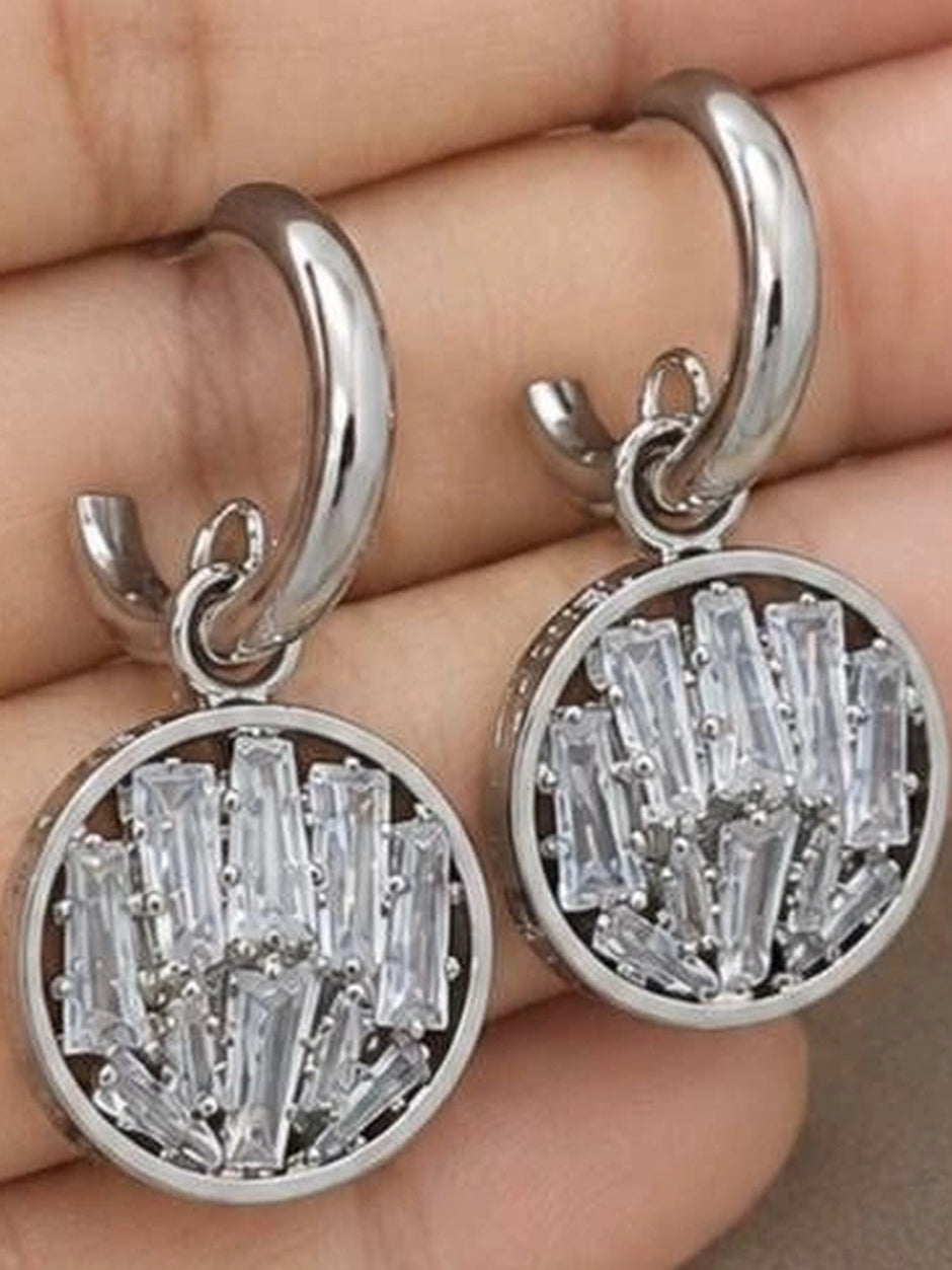 Close-up of silver circular drop earrings held in palm showing baguette crystal cluster detail