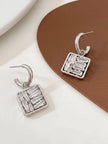 Single silver hoop earring with square baguette zirconia charm shown front and back on a brown tray