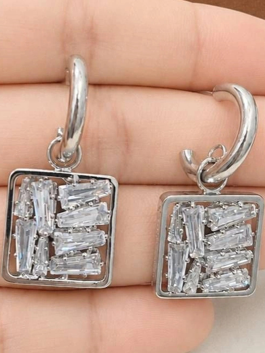 Close-up of both square baguette zirconia drop earrings held in an open palm showing stone clarity