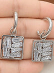 Close-up of both square baguette zirconia drop earrings held in an open palm showing stone clarity