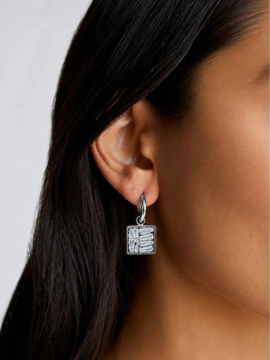 Model wearing one silver square baguette zirconia drop earring on pierced ear with dark hair