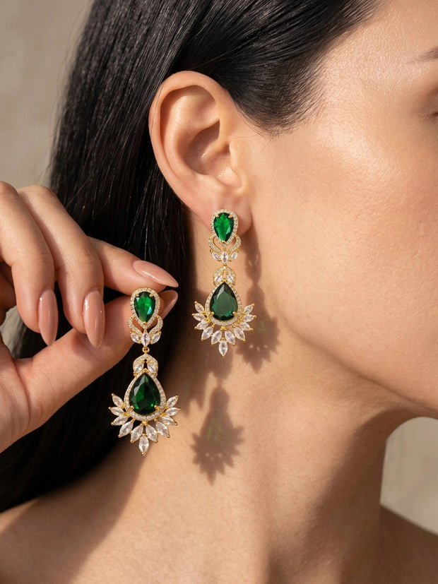 Woman wearing gold-plated emerald green CZ teardrop drop earrings against her ear, held in hand