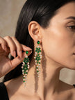 Pair of emerald green and clear stone floral drop earrings laid flat on white surface