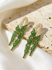 Two gold-plated emerald CZ tassel earrings resting on a textured stone surface in bright natural light