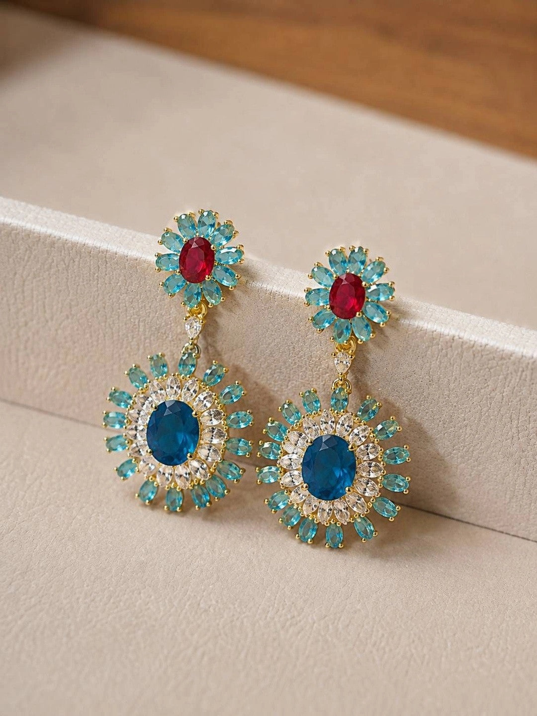 Close-up of crystal sunburst drop earrings resting against a cream display box edge