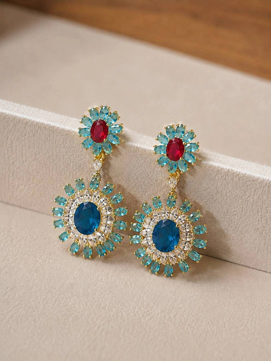 Close-up of crystal sunburst drop earrings resting against a cream display box edge