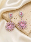 Pair of pink crystal sunburst drop earrings laid on a beige stone surface with cream satin fabric