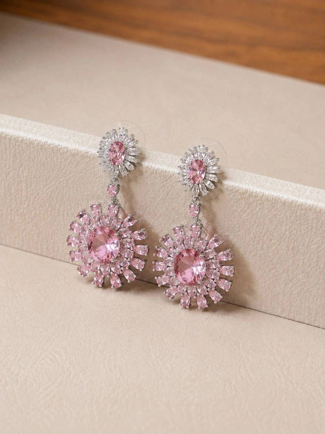 Close-up of pink floral drop earrings propped against a cream jewellery box edge showing push-back backs