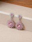 Close-up of pink floral drop earrings propped against a cream jewellery box edge showing push-back backs